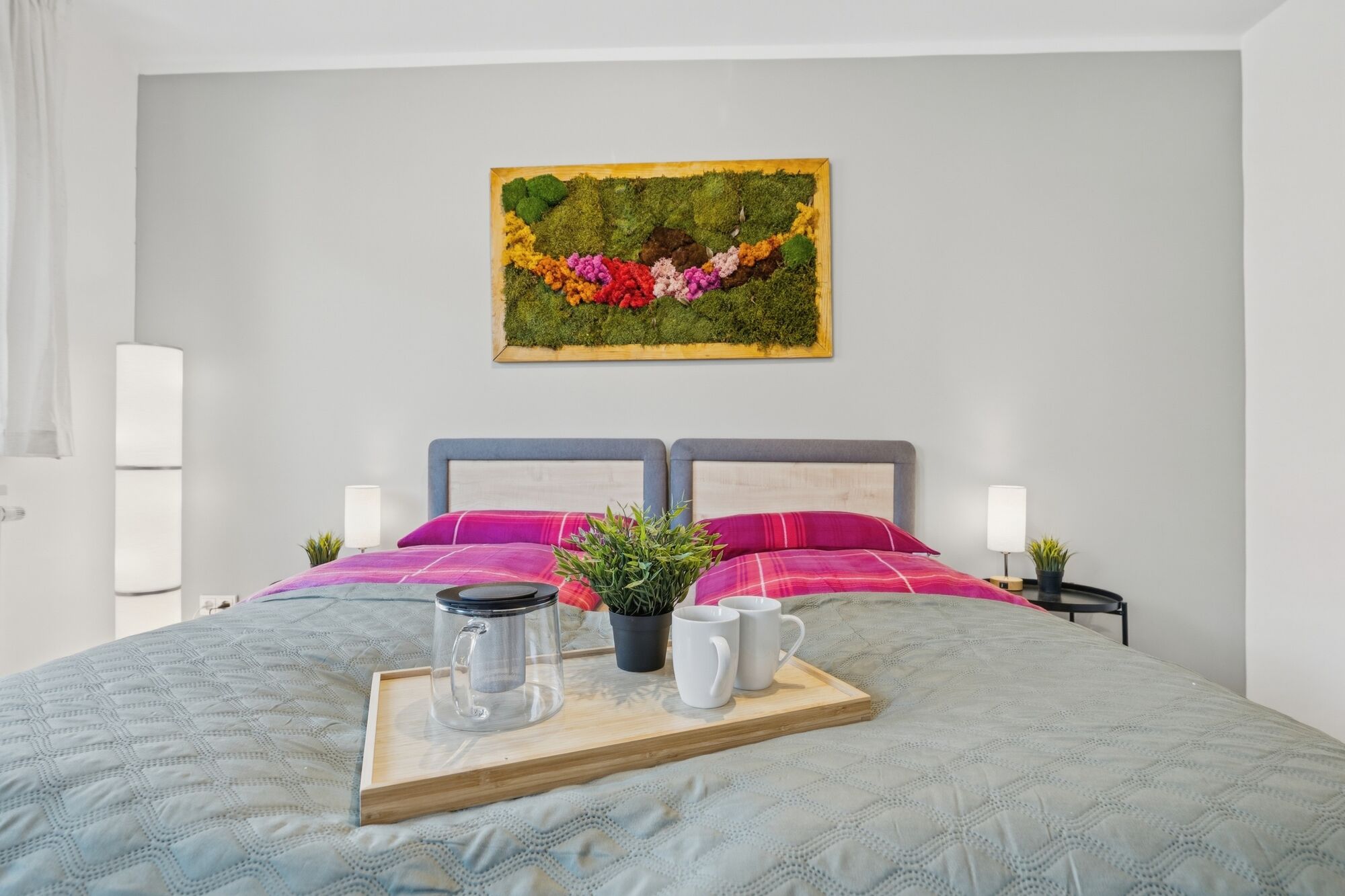 Doppelbett mit pinker Bettwäsche, buntes Moosgemälde an der Wand, Frühstückstablett auf dem Bett. Doppelbett mit pinker Bettwäsche, buntes Moosgemälde an der Wand, Frühstückstablett auf dem Bett.