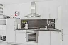 Weiße Küche mit dunkler Rückwand, Ceranfeld, Backofen, Wasserkocher und Wanduhr. Weiße Küche mit dunkler Rückwand, Ceranfeld, Backofen, Wasserkocher und Wanduhr.