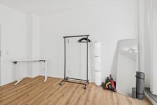 Schwarzer Kleiderständer auf Rollen, weiße Wände, heller Holzboden, viel Platz. Schwarzer Kleiderständer auf Rollen, weiße Wände, heller Holzboden, viel Platz.