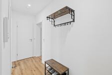 Heller Flur mit schwarzem Wandregal, Holzbank mit Schuhen, schlichte weiße Wände. Heller Flur mit schwarzem Wandregal, Holzbank mit Schuhen, schlichte weiße Wände.