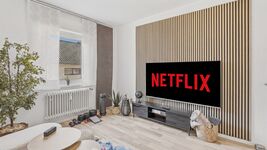 Helles Wohnzimmer mit großem Flachbildschirm, Netflix-Logo, Holzlamellenverkleidung und Zimmerpflanz Helles Wohnzimmer mit großem Flachbildschirm, Netflix-Logo, Holzlamellenverkleidung und Zimmerpflanz