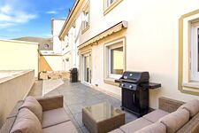 Gepflasterte Innenhofterrasse mit Rattan-Loungesessel, Gasgrill, Markise, helle Fassade. Gepflasterte Innenhofterrasse mit Rattan-Loungesessel, Gasgrill, Markise, helle Fassade.