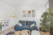 Blaues Sofa mit Kissen, runde Beistelltische, goldene Wandleuchte, heller Holzboden. Blaues Sofa mit Kissen, runde Beistelltische, goldene Wandleuchte, heller Holzboden.