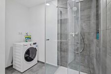 Graue Fliesendusche, Einbauwaschmaschine daneben, moderne Armaturen, helle Beleuchtung. Graue Fliesendusche, Einbauwaschmaschine daneben, moderne Armaturen, helle Beleuchtung.