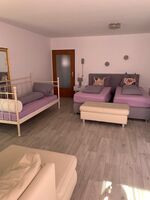 Wohn-Schlafzimmer mit zwei bequemen Boxdpringbetten und einem Einzelbett, eine Couch. Balkonzugang. 