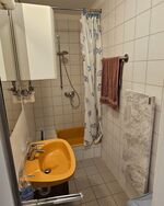 kleines Gemeinschaftsbadezimmer mit Dusche, Heizstein, Waschbecken und Spiegel. 