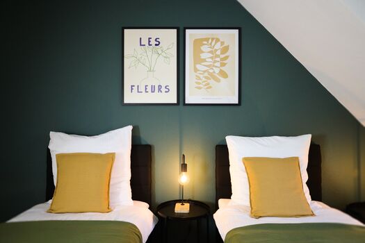 Schlafzimmer 1 - Twin-Schlafzimmer mit zwei Einzelbetten, hochwertiger Bettwäsche, TV, Nachttischlampen und ruhigen Grüntönen.