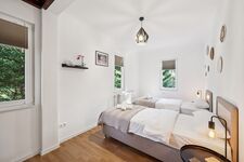 Schlafzimmer 1 mit hochwertigen Boxspringbetten, Nachttischen und einem offenen Kleiderschrank sowie Blick ins Grüne. Die Betten können wahlweise einzeln oder als komfortables Doppelbett gestellt werden.