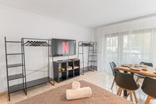 Helles Wohn- und Esszimmer mit 55 Zoll Smart-TV. Offene Kleiderständer und Regale bieten ausreichend Stauraum für längere Aufenthalte. Viel Tageslicht durch große Fensterfront.