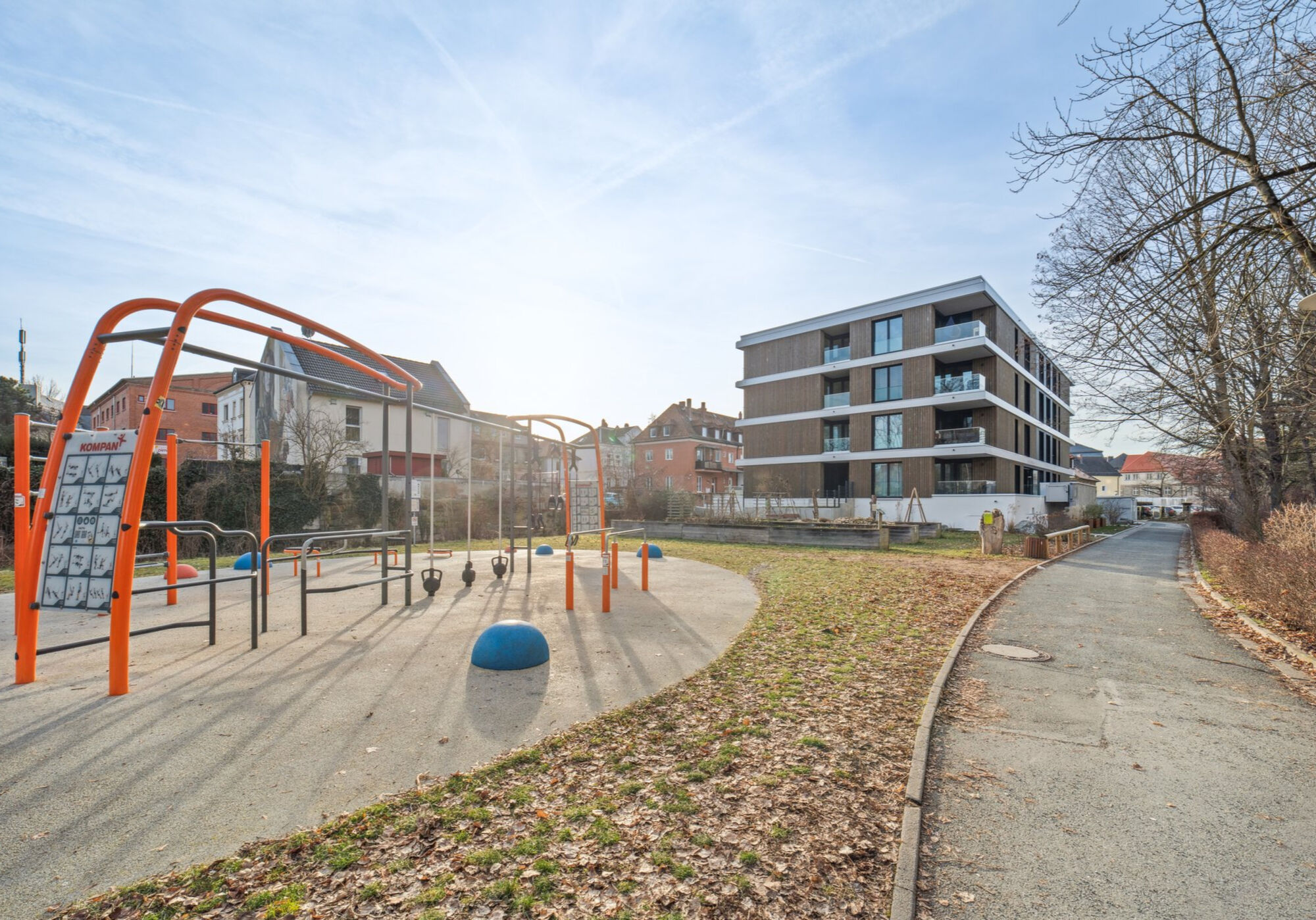 Auf das rechteckige, braun/weiße Haus blickend: Rechts vom Haus befindet sich der Haupteingang. Links vom Haus befindet sich die Einfahrt in die Tiefgarage.