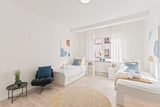 4-Zimmer-Wohnung: Zimmer 3 - Helles Zweibettzimmer mit zwei Einzelbetten. Ausgestattet mit Nachttischen, Sessel, Stauraum und 40 Zoll Smart-TV. Große Fenster sorgen für viel Tageslicht.