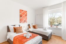 3-Zimmer-Wohnung: Zimmer 1 – Helles Zimmer mit zwei Einzelbetten. Ausgestattet mit 40 Zoll Smart-TV, Schreibtisch, Stuhl und Stauraum. Große Fenster sorgen für viel Tageslicht.